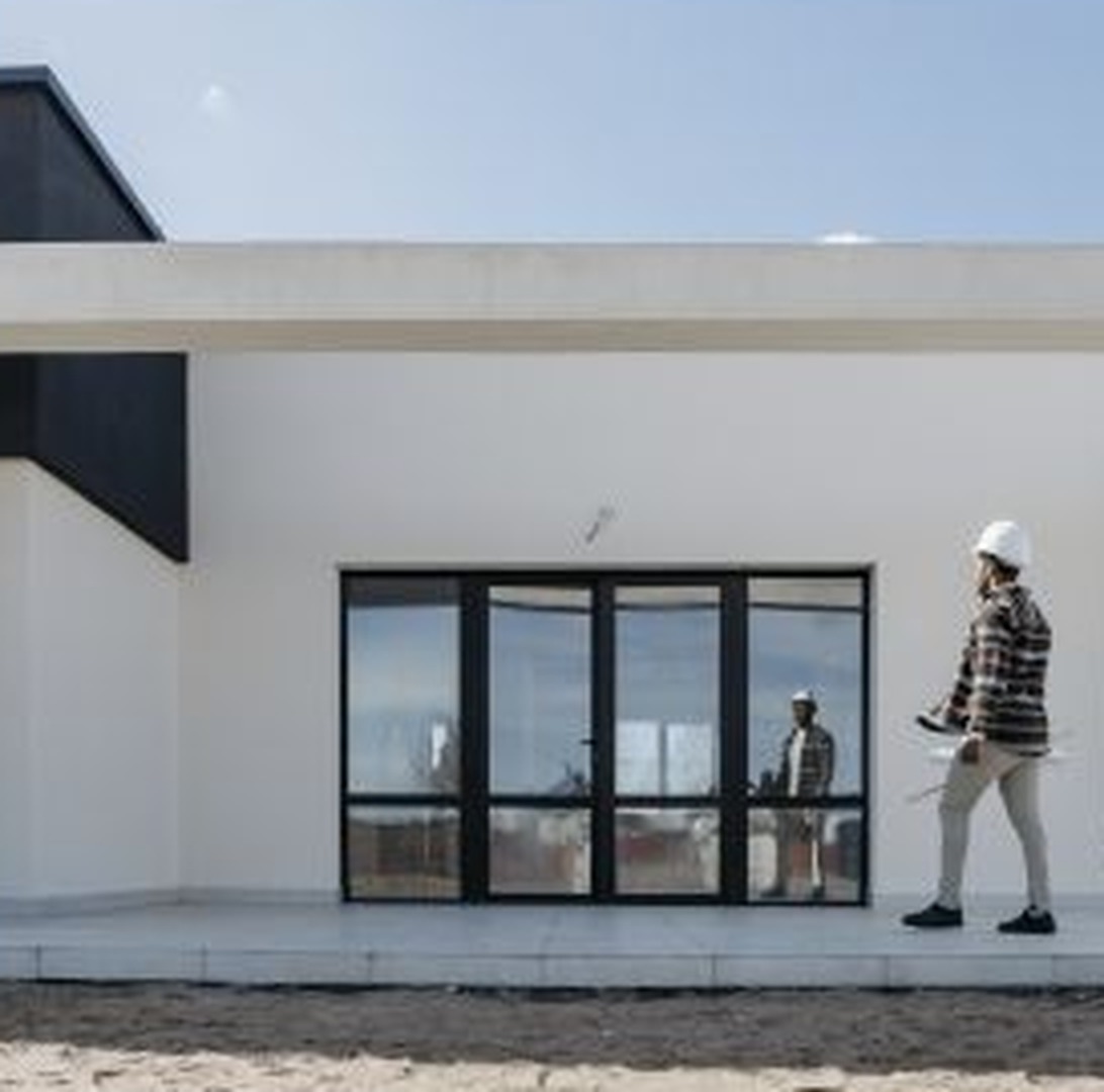 Modern white home exterior with a builder walking past the glass entry